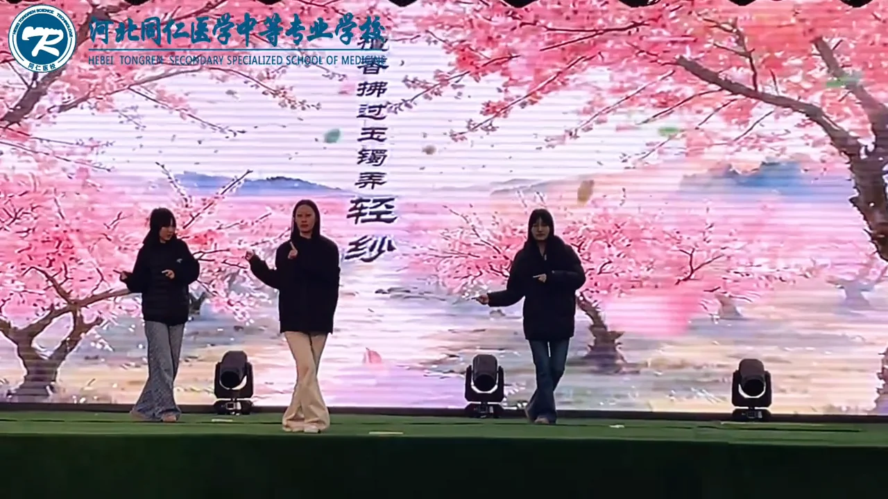 三名学生在樱花背景屏前表演舞蹈片段
